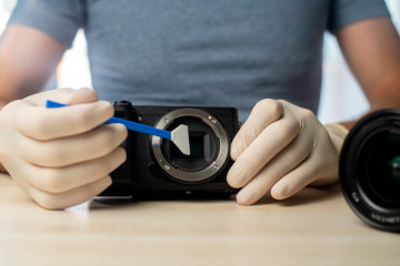 Person cleaning mirrorless digital camera with gloves on and swab. Technology concept