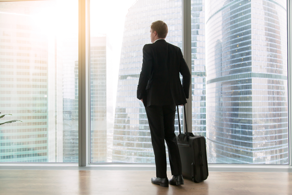 Young,Businessman,With,Suitcase,Standing,Looking,At,Full,Length,Window,