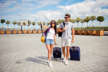 Two,Smiling,Young,Lovers,With,Valise,Walking,From,Airport,In