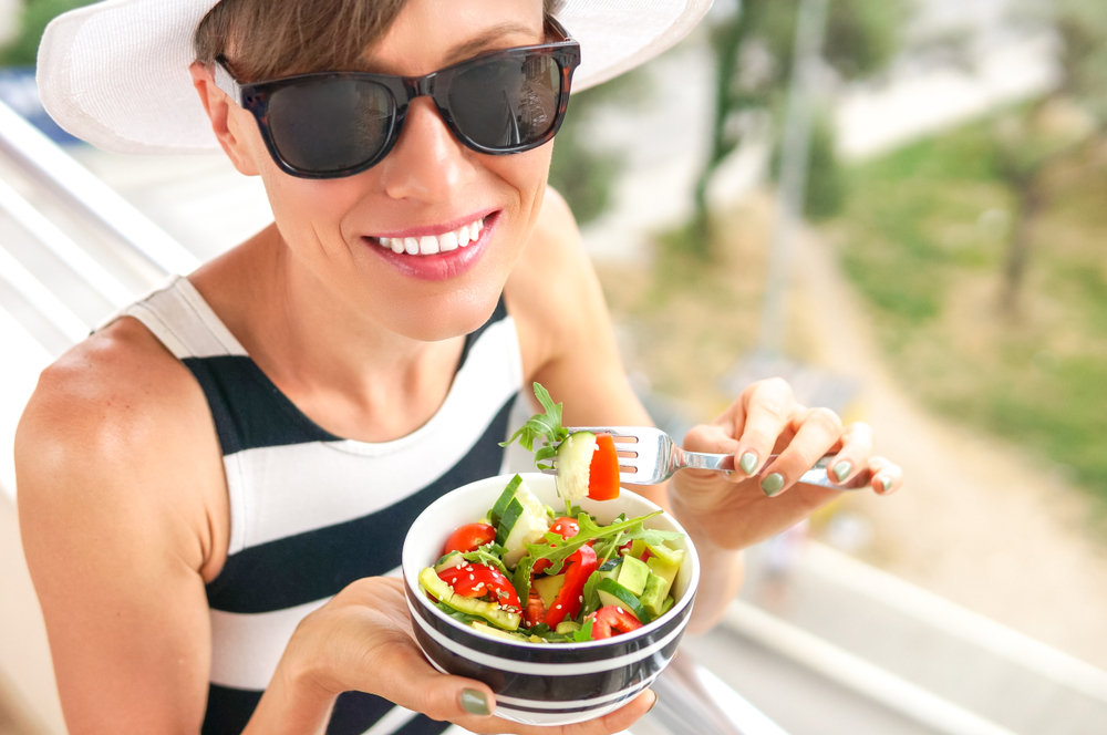 Young,Woman,Eating,Salad,While,Staning,On,A,Balcony