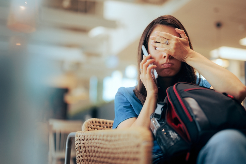 Unhappy,Woman,Talking,On,The,Phone,Waiting,In,An,Airport