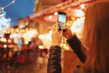 Woman,Taking,Pictures,Of,European,Christmas,Market,Scene,On,Smartphone.