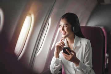 Cheerful,Female,Passenger,In,Headphones,For,Noise,Cancellation,Watching,Online